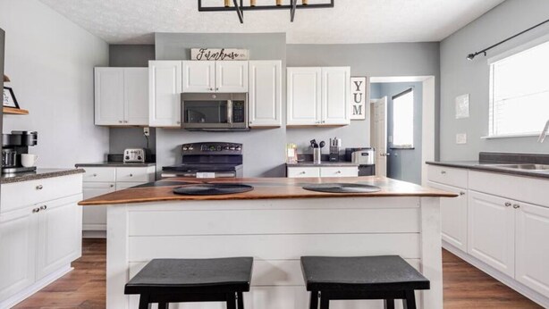 Una cocina moderna con armarios blancos, una isla central con taburetes, un microondas y un tostador.