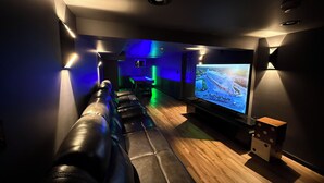 Una sala de cine en casa con sofá de cuero, televisor de pantalla plana grande e iluminación ambiental.