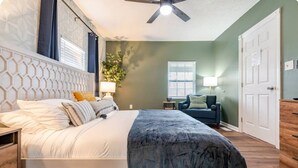 Un dormitorio con cama, ventilador de techo, ventana, puerta y una mesita de noche con lámpara.