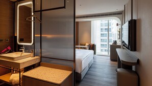 A modern hotel room with a large bed, a sitting area, a bathroom with a sink and mirror, and a view of the city through large windows. - 采寓halo house (Taichung)