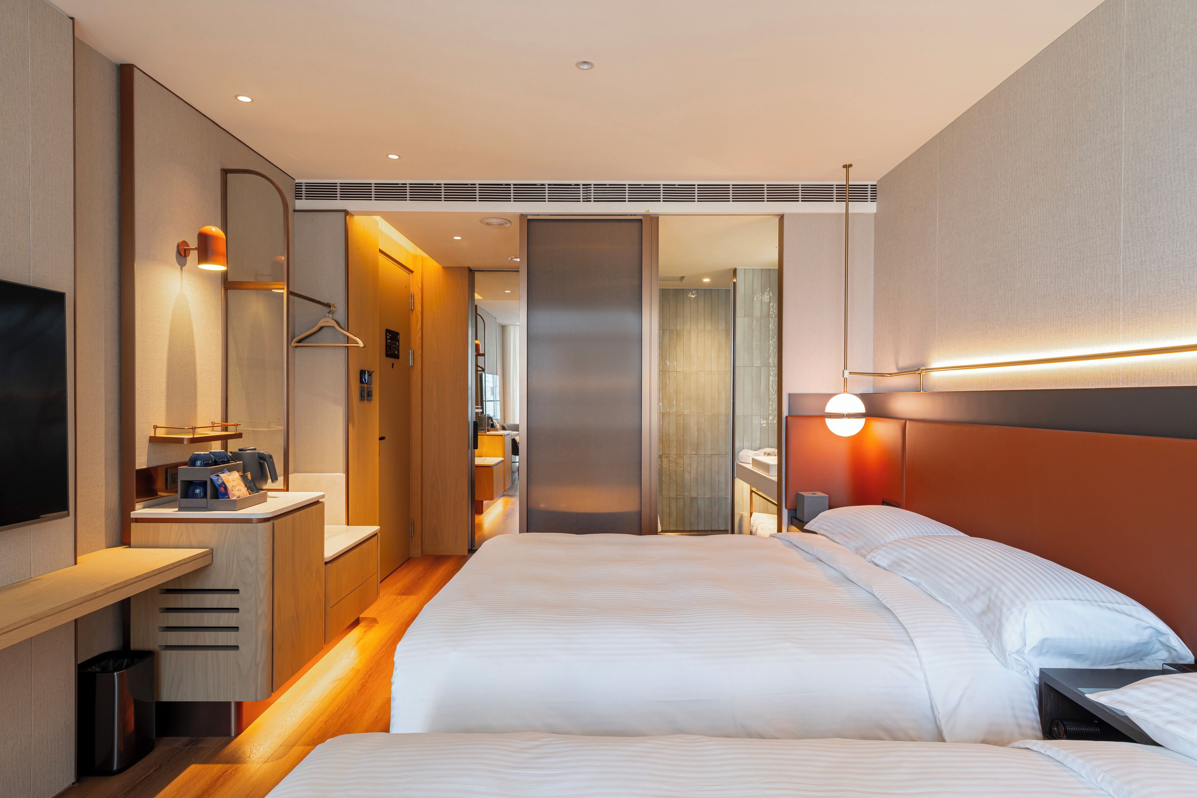 Una habitación de hotel moderna con una cama grande, un escritorio con televisor de pantalla plana y un baño con espejo y perchero para toallas.