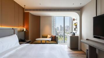 Una habitación de hotel moderna con una cama grande, una zona de estar, un televisor y vistas a la ciudad.