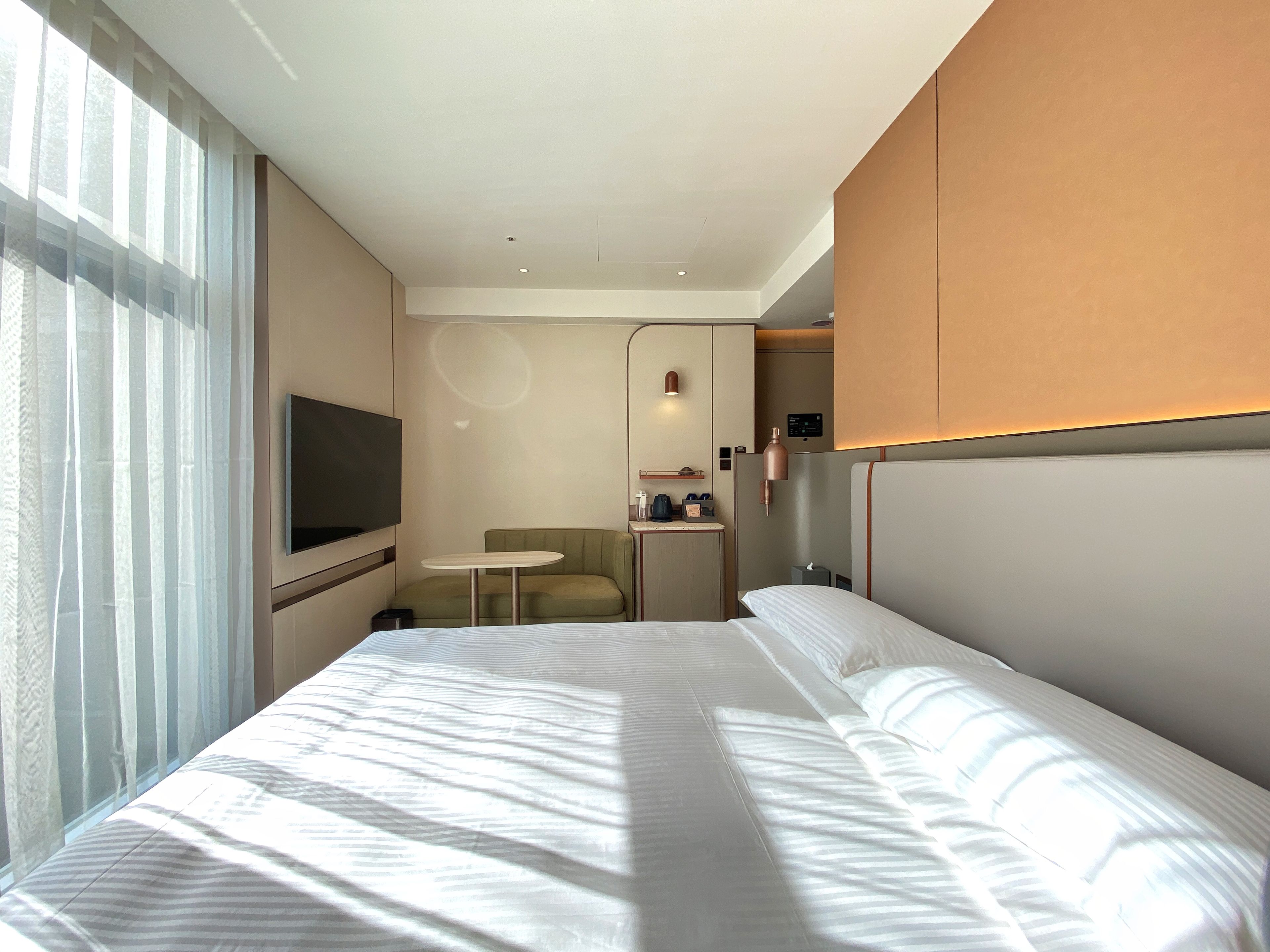 Una habitación de hotel con una cama grande, un televisor en la pared, una mesita y una silla.