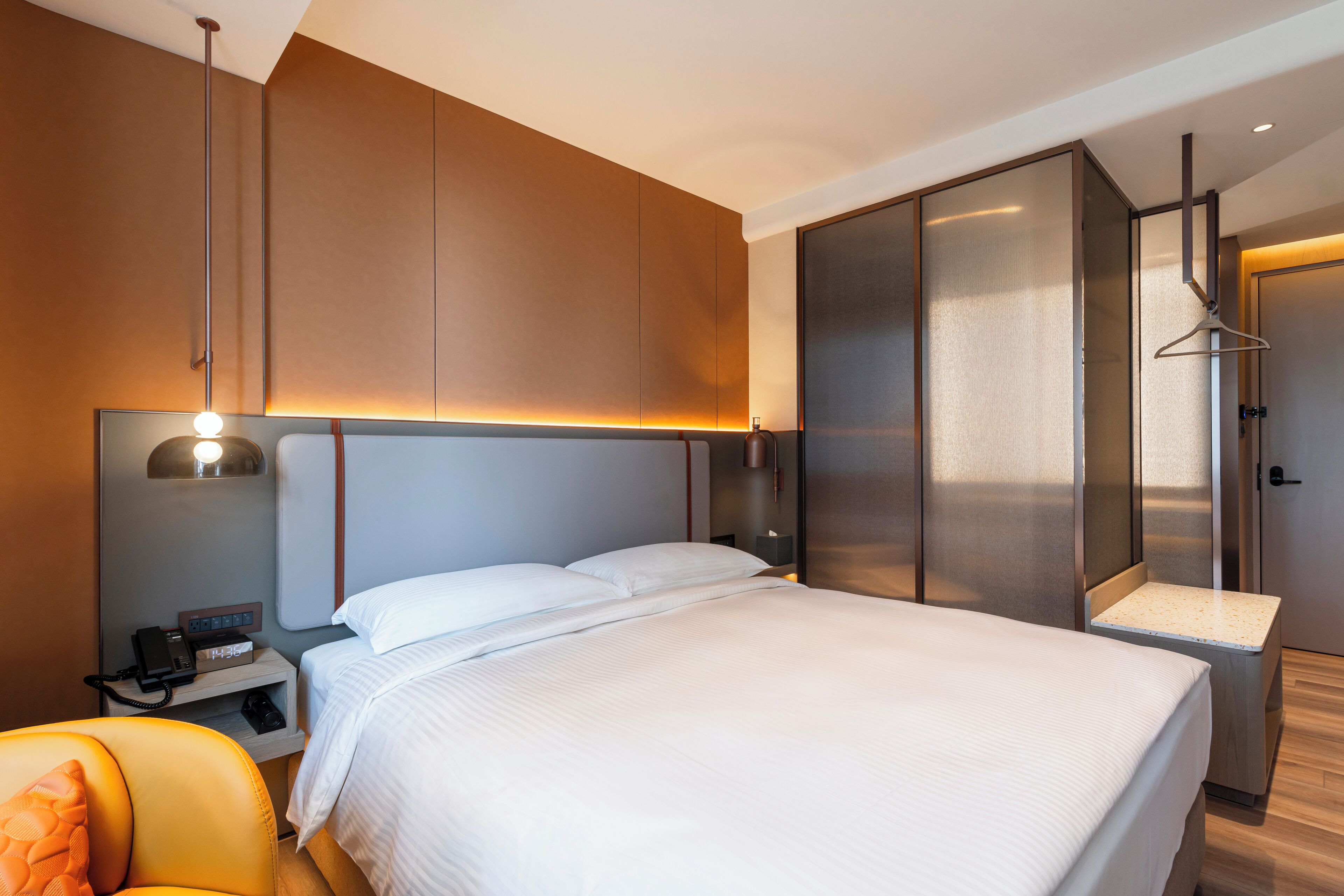 Una habitación de hotel moderna con una cama grande, una mesita de noche con lámpara, una silla y un armario.