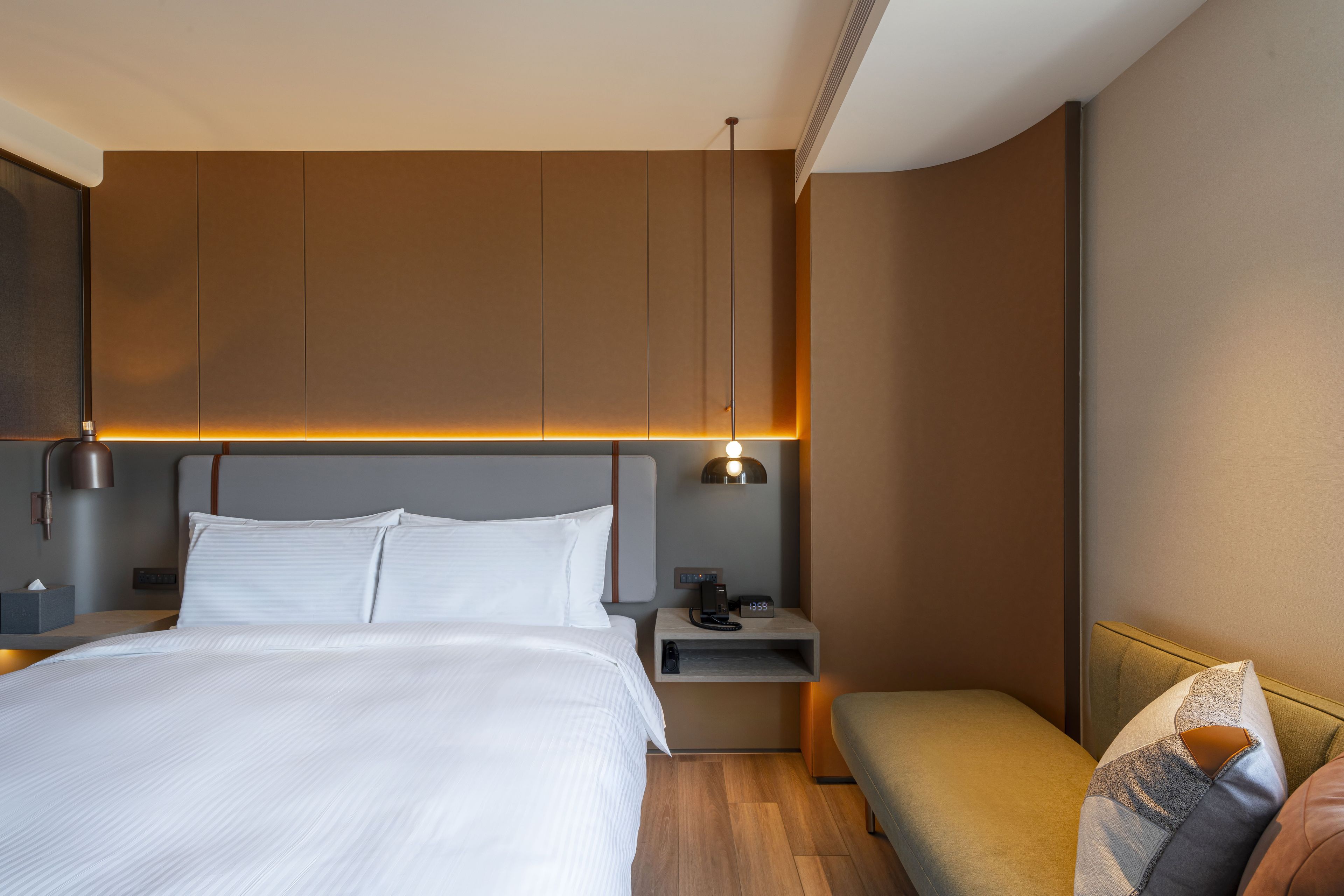 A modern hotel room with a large bed, bedside tables, a nightstand, a bench, and a wall-mounted lamp.
