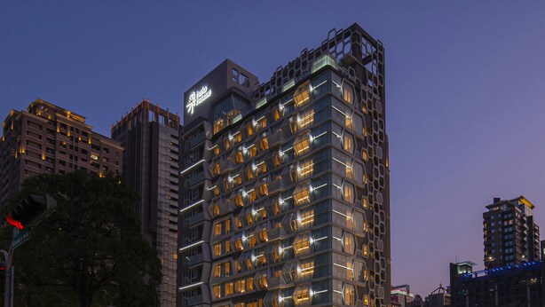 A modern high-rise building with a distinctive geometric facade and illuminated windows. - 采寓halo house (Taichung)