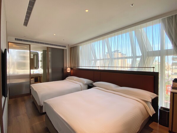 Habitación de hotel con dos camas, un ventanal con cortinas, un espejo y un calentador de pared.