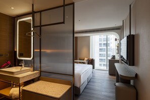 A modern hotel room with a large bed, a sitting area, a bathroom with a vanity, and a large window offering a city view. - 采寓halo house (Taichung)