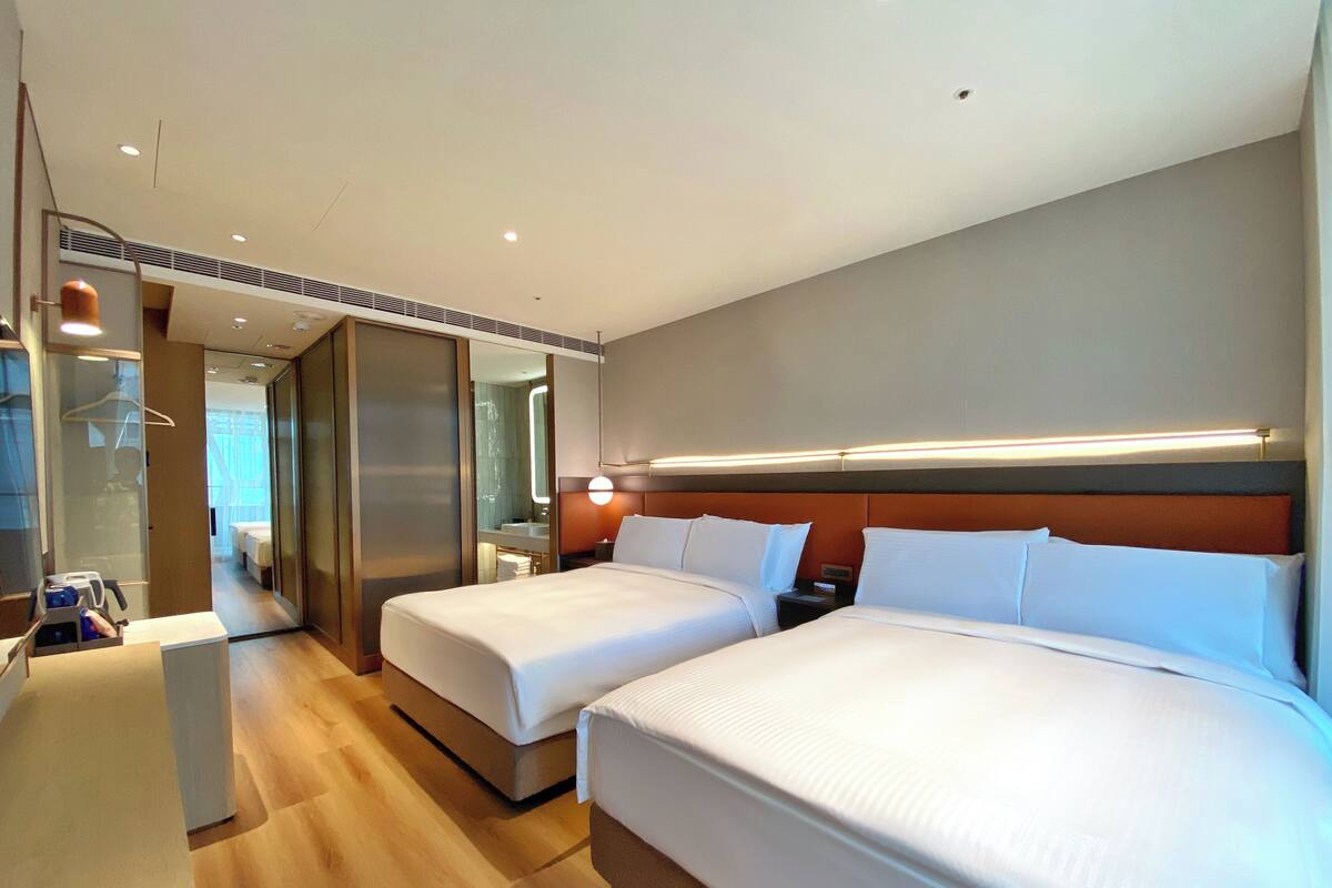 A hotel room with two beds, a large mirror, a wooden floor, and a modern design.