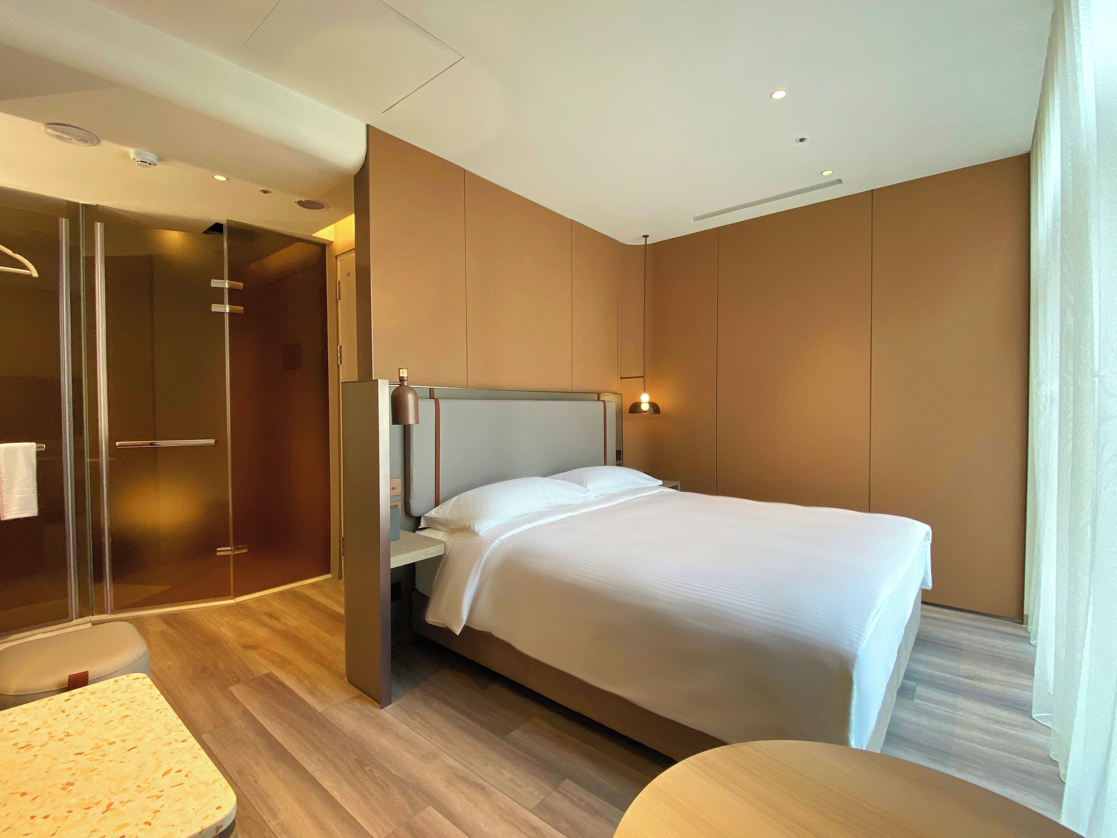 A modern hotel room with a bed, a glass shower enclosure, and a wooden floor.