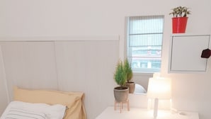 Une chambre bien rangée, avec un lit, un bureau blanc, une chaise et deux plantes en pot.