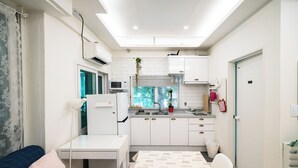 Une cuisine compacte avec des meubles blancs, un four à micro-ondes et un évier. On y trouve une table à manger recouverte d’une nappe à motifs et un canapé bleu agrémenté d’un coussin.