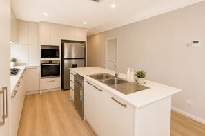 A modern kitchen with white cabinetry, stainless steel appliances, a double sink, and a small potted plant. - 5 O Clock Somewhere (West Busselton)