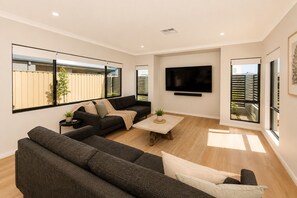 A modern living room with a sectional sofa, a coffee table, and a flat-screen TV mounted on the wall. - 5 O Clock Somewhere (West Busselton)