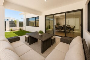 An outdoor patio with a table and chairs, a grassy lawn, and a sliding glass door leading to an interior dining area. - 5 O Clock Somewhere (West Busselton)