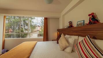 A hotel room with a large window, a wooden headboard, and a bed with white bedding and striped pillows.