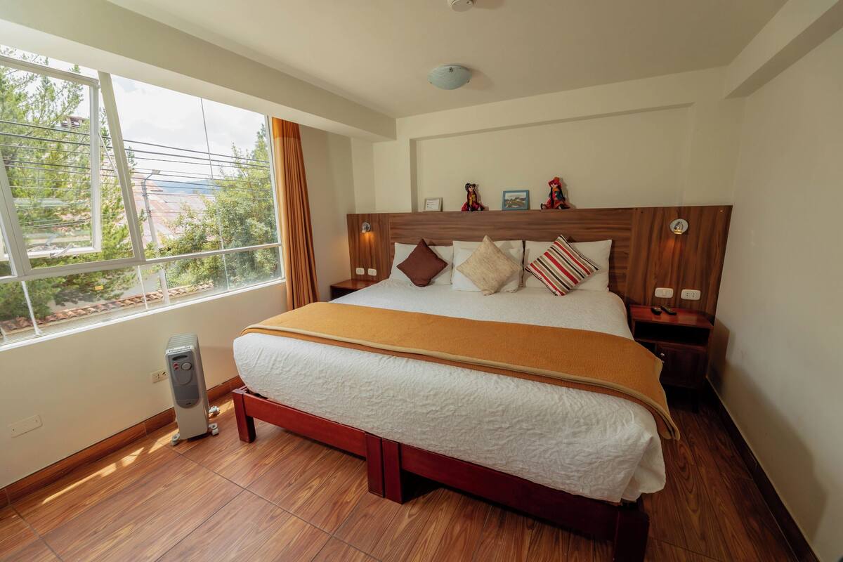 A hotel room with a large bed, wooden headboard, bedside tables, and a window with curtains.
