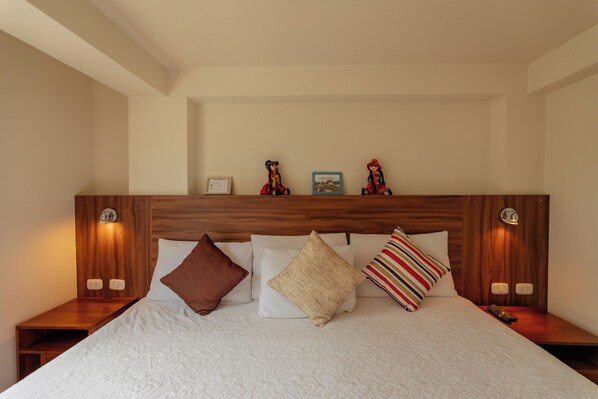 Uma cama bem arrumada com cabeceira de madeira, vários travesseiros e abajures.