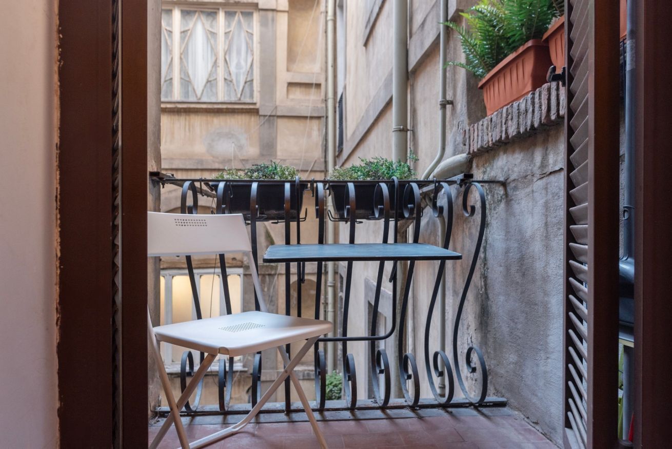 A small outdoor balcony with a metal railing, a white folding chair, and a table.
