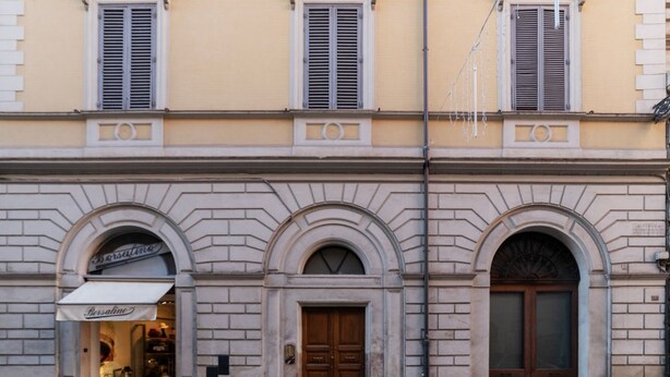 A building with three arched doorways, a shop entrance with awning, and a street lamp. - GuestHost - Charming Apartment near Spanish Steps (Rome)