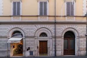 Un edificio con tres arcos, una entrada de tienda con toldo y un farol.