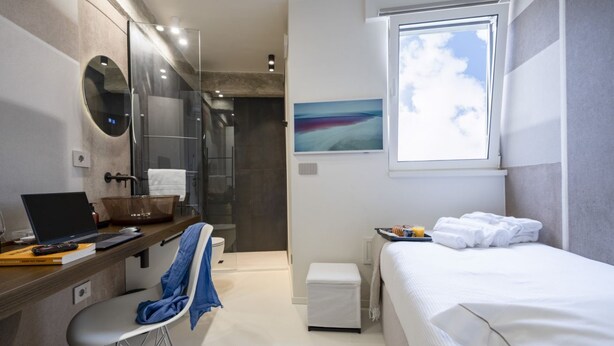 A modern hotel room with a shower, a desk with a laptop, a bed, and a window with a view.