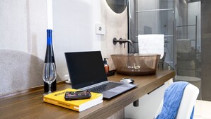 A modern bathroom with a glass shower, a wooden vanity, a laptop, a book, and a wine glass.
