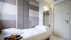 A hotel room with a bed, a tray with breakfast items, a wardrobe, and an air conditioning unit.