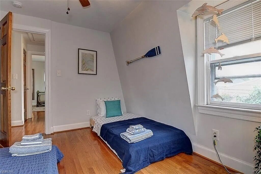 A bedroom with a bed, a window with blinds, a wall-mounted paddleboard, and a door leading to another room.