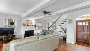 A spacious living room with a white leather sofa, a fireplace, a television, and a staircase leading to another level.