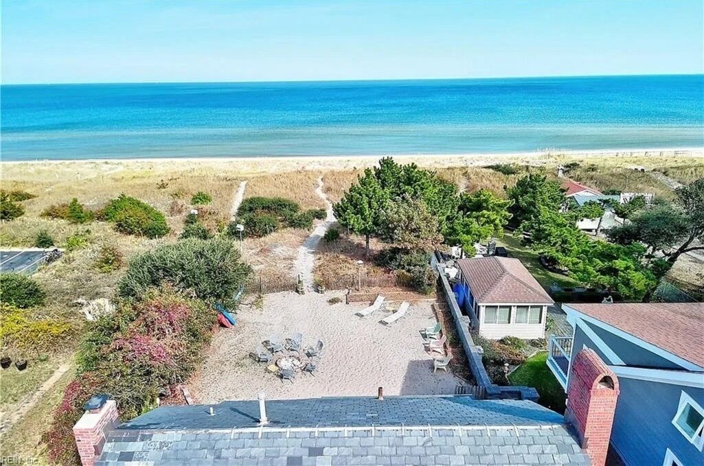 A beach view with a patio area, lounge chairs, and a small building.