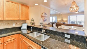 A modern kitchen with wooden cabinets, a granite countertop, a stainless steel sink, and a pendant light.