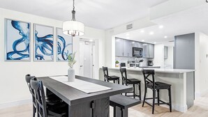 Una cocina moderna con gabinetes blancos, una isla central y una zona de comedor con una mesa y sillas de madera oscura.