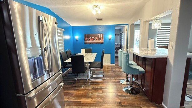 A modern kitchen with a stainless steel refrigerator, a dining area with a table and chairs, and a bar area with stools. - Newly updated home on Spruce St (Mason)