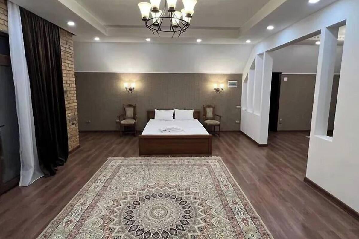 A spacious bedroom with a large bed, two chairs, a patterned rug, and a chandelier.