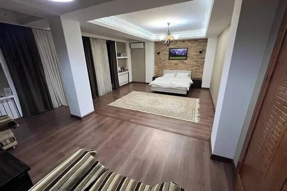 A modern bedroom with a large bed, a flat-screen TV mounted on a brick wall, and a ceiling light fixture.