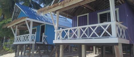 Two beach houses with wooden stilts, blue and purple exteriors, and white railings.