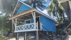 Un edificio pequeño de un solo piso con fachada azul y balcón blanco, rodeado de palmeras.