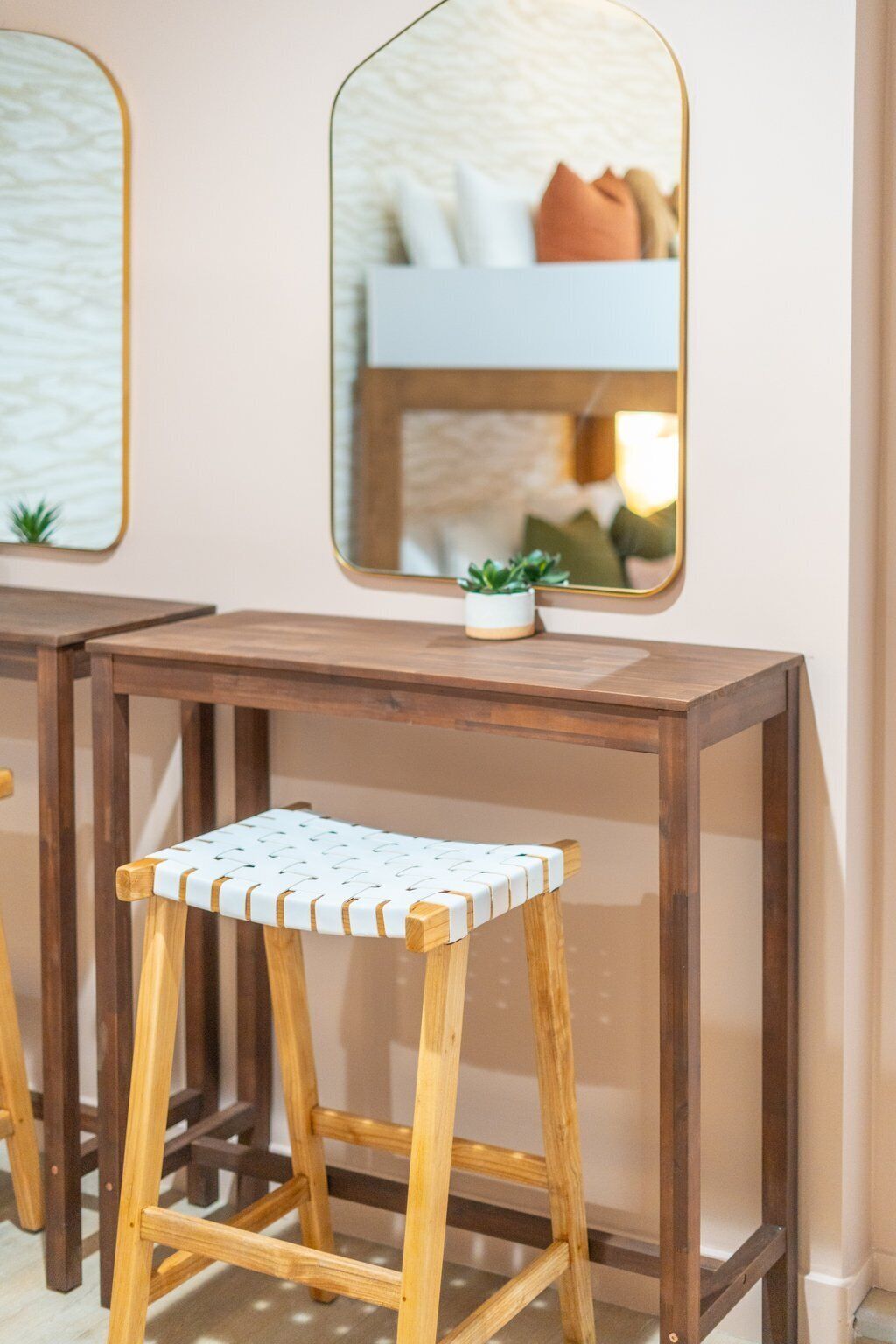 A wooden stool with a woven seat, a small potted plant, and a mirror on a wall.