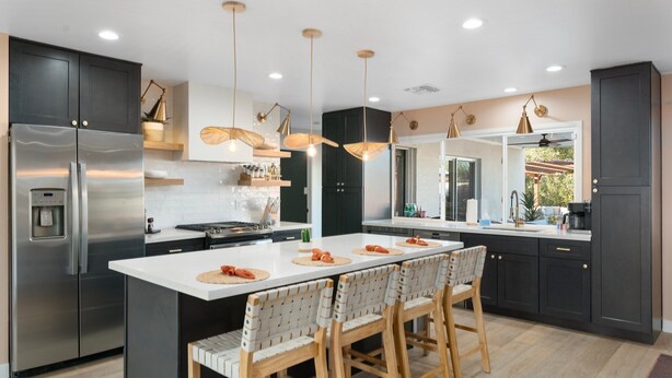 Een moderne keuken met een centraal eiland, donkere kastjes, roestvrijstalen apparatuur en hangende lampen.