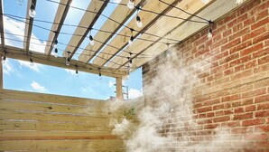 A hot tub with steam rising from the water, surrounded by a wooden deck and a brick wall. - Luxury Private Boutique Hotel with CityView, Hot Tub, Free Parking (Pittsburgh)
