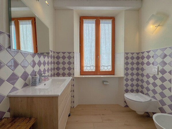 A bathroom with a sink, toilet, and window.