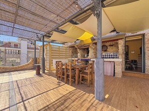 Un patio al aire libre con mobiliario de madera, una chimenea de piedra y una zona cubierta con techo de paja.