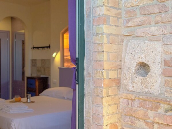 A hotel room with a bed, a nightstand, and a wall with a brick pattern and a small hole.