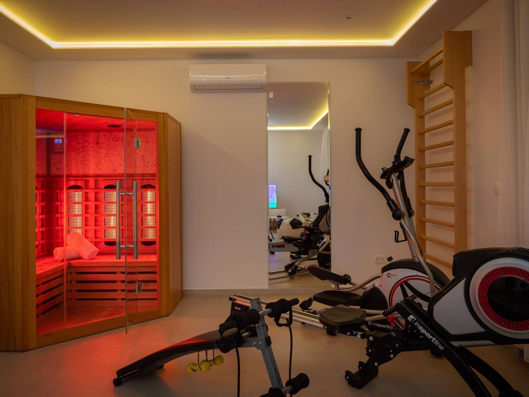 A home gym with exercise equipment, a sauna, and a wooden bench.