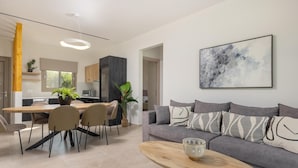 A modern living room with a grey sofa, a wooden coffee table, and a dining area with a wooden table and chairs. - Villa Ismini Periyali (Zakynthos)