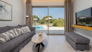 A modern living room with a grey sofa, a wooden coffee table, and a TV mounted on the wall. - Villa Ismini Periyali (Zakynthos)