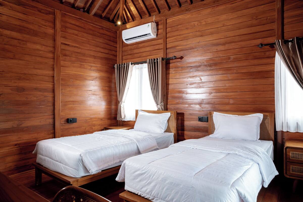 Une chambre de style cabane en bois, équipée de deux lits, d’un ventilateur de plafond et d’un appareil de climatisation.