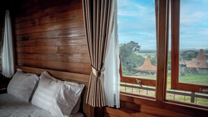 Ein Holzhüttenraum mit Bett, Vorhängen und einem Fenster mit Blick auf ein Dorf.