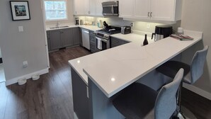Una cocina moderna con armarios blancos, una isla central con taburetes altos, un microondas y una estufa.
